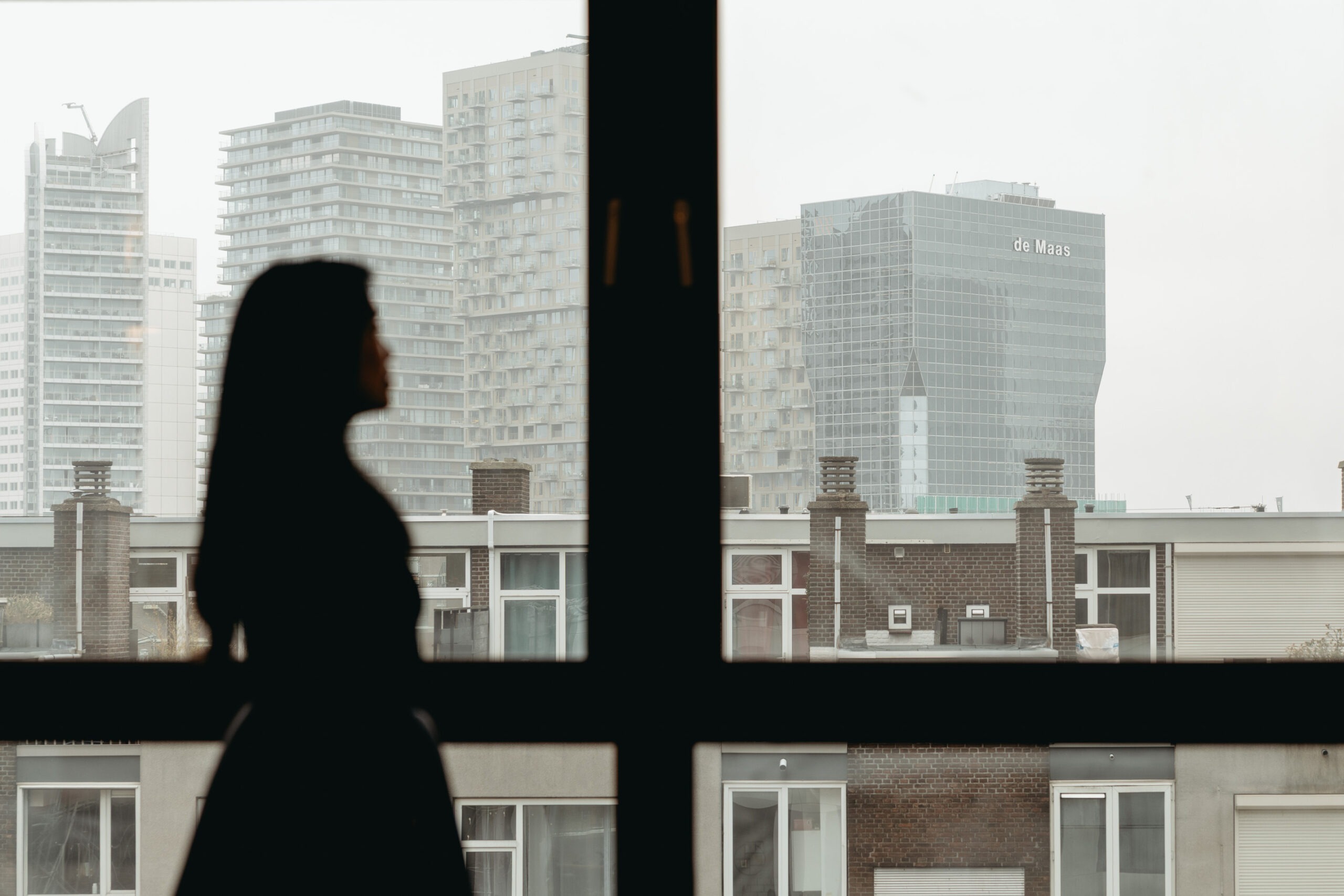 Yeh Design interior designer silhouetted against Rotterdam city skyline viewed through apartment window during client project site visit