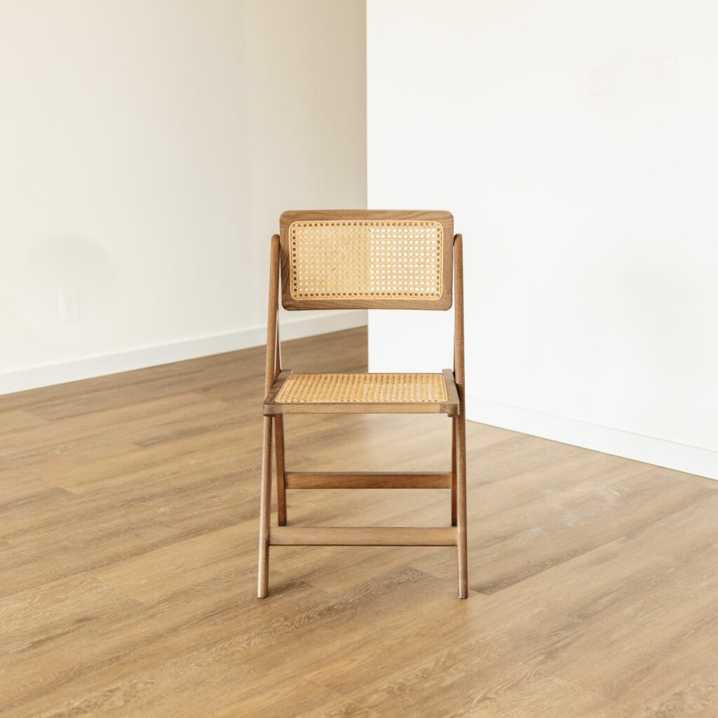 Walnut folding chair with cane seat and back on oak herringbone floor against white wall