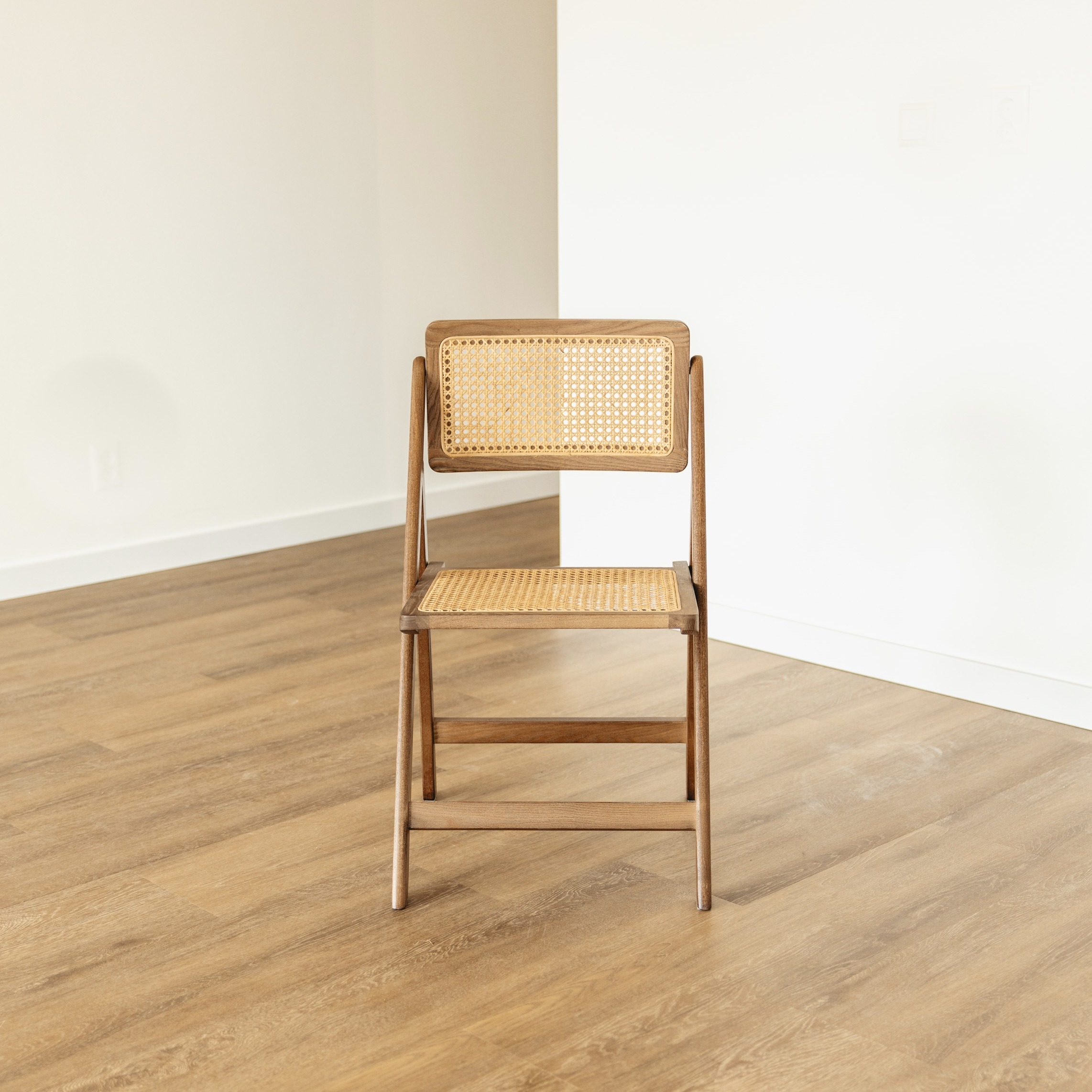 Walnut folding chair with cane seat and back on oak herringbone floor against white wall