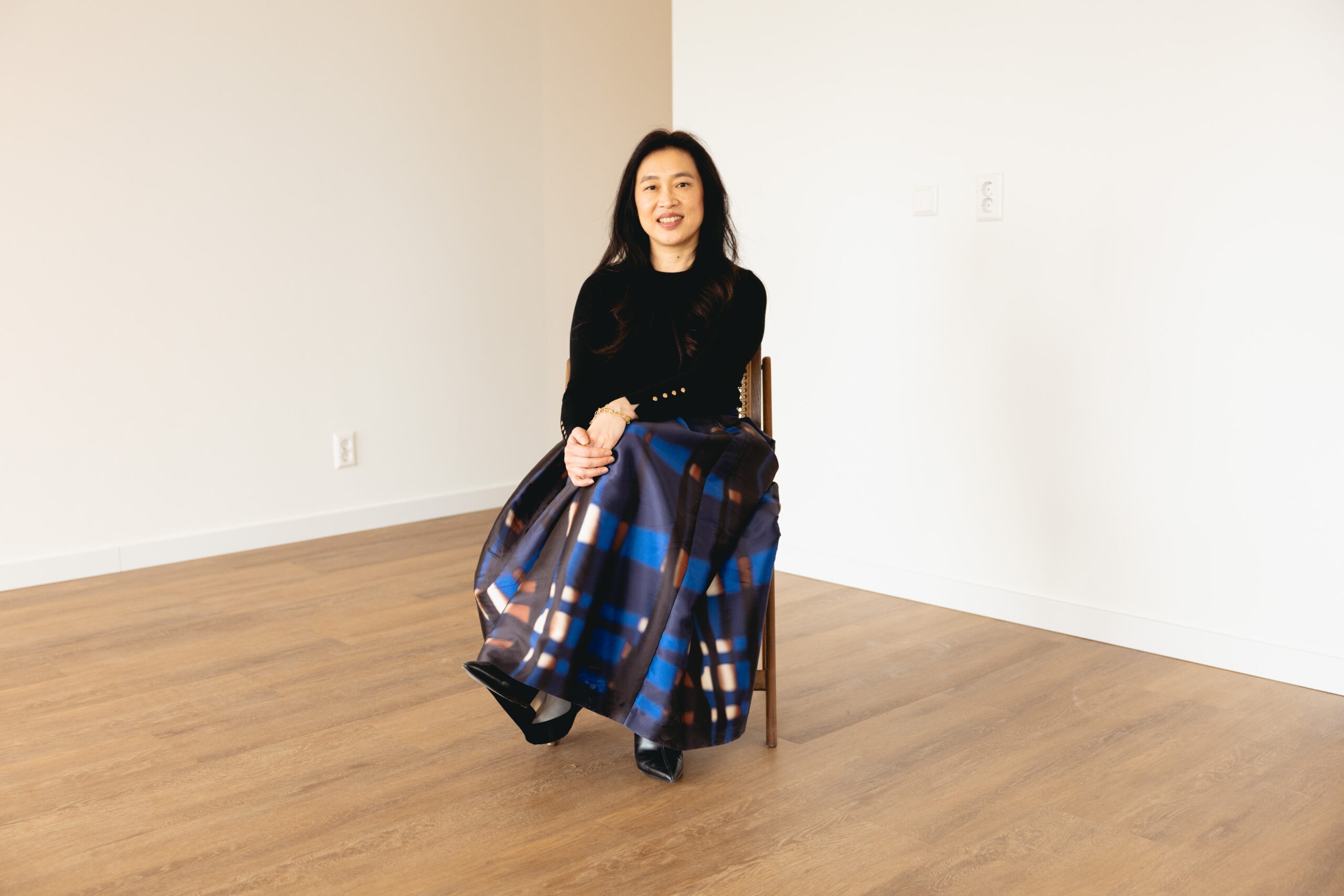 Yeh Design founder portrait seated on cane chair in empty white room with oak floor