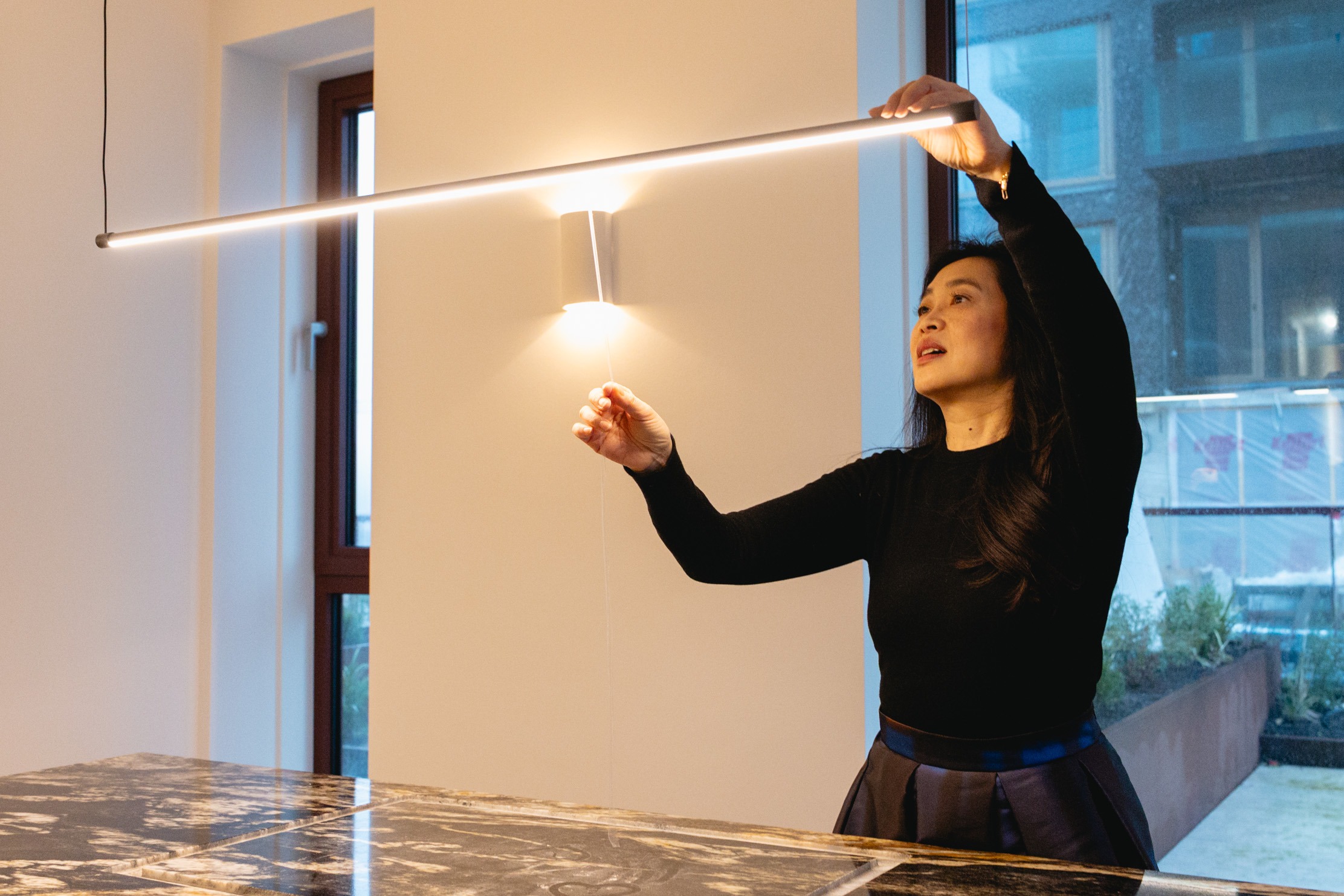 Yeh Design interior designer adjusting pendant tube light position above marble kitchen island during project installation