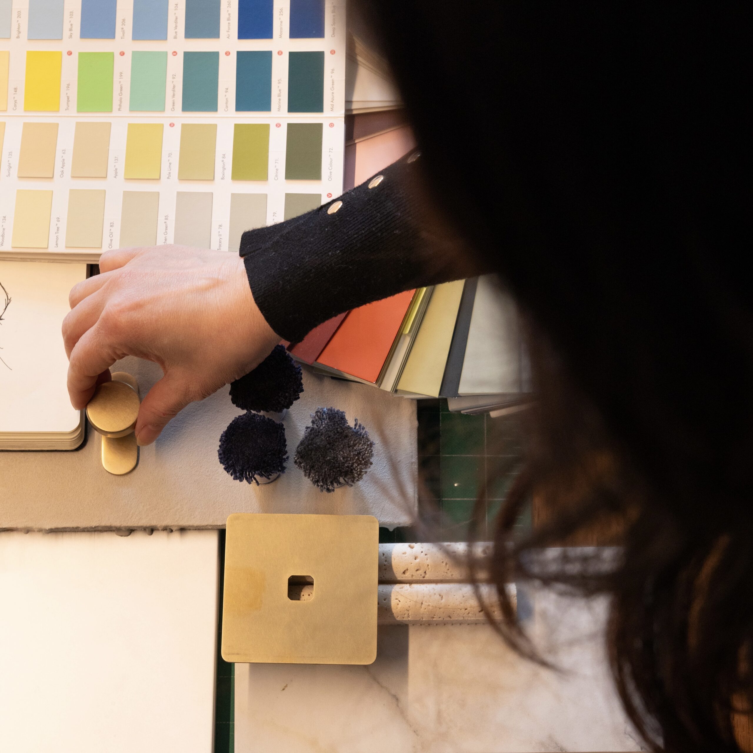 Interior designer reviewing material samples and colour swatches on studio desk, including brass hardware and stone tiles