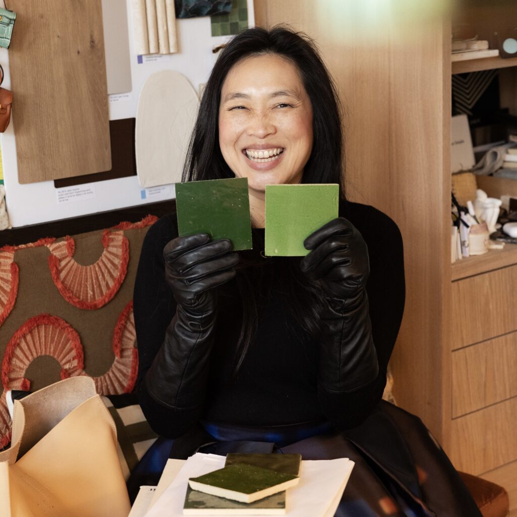 Hsiu-Li, founder od Yeh Design, smiling and holding two green tile samples in interior design studio